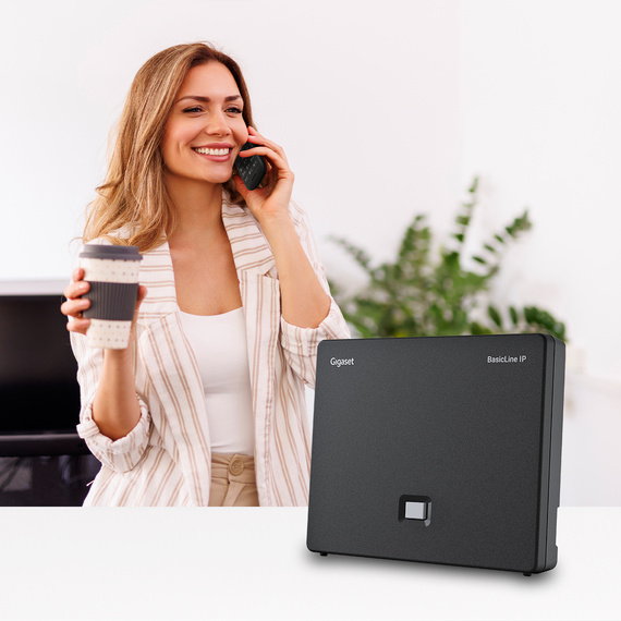 Stacja bazowa Gigaset BasicLine IP w domowym biurze z użytkowniczką podczas rozmowy telefonicznej