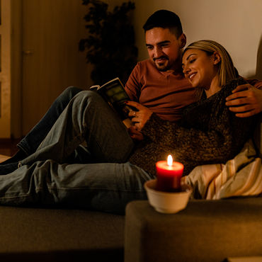 Couple sitting comfortably on the sofa in the living room in the evening with a book and candlelight.