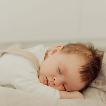 Sleeping baby in a white romper suit, lying peacefully on a soft blanket.
