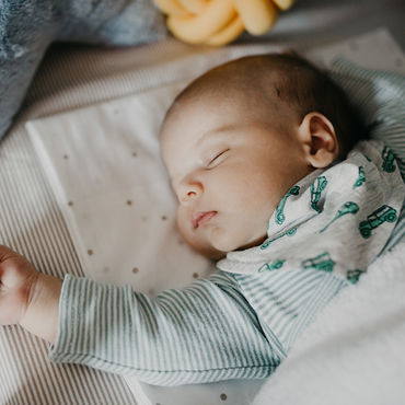 Neonato con una sciarpa fantasia dorme tranquillamente nella sua comoda culla.