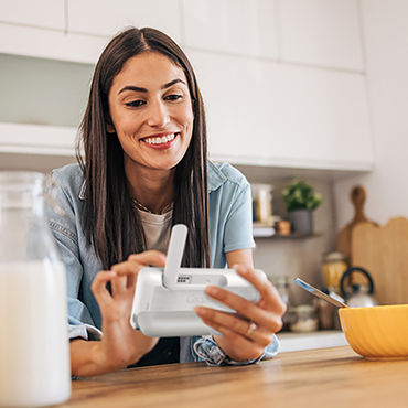 Una donna è in cucina e utilizza il baby monitor Gigaset con un sorriso.
