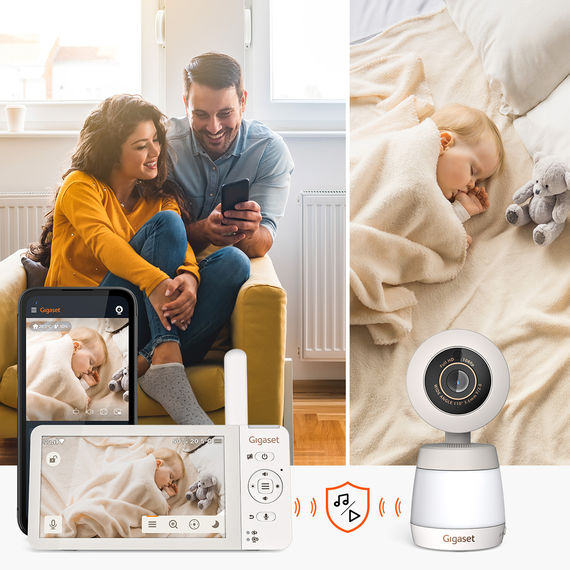 Eltern sehen aufs Smartphone, Monitor zeigt Babyaufnahme; Gigaset BABY 700 Connected Kamera im Vordergrund.