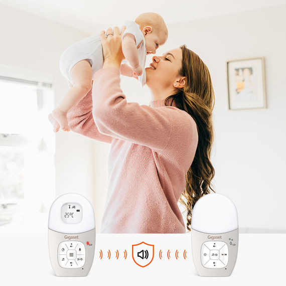 Babyphone mit Eltern- und Babyeinheit. Im Hintergrund eine junge Mutter, die ihr Baby auf dem Arm hält.