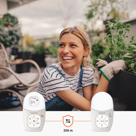 Baby monitor con unità genitore e bambino. Sullo sfondo, una giovane donna in giardino con un cane.