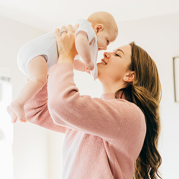 Una mamma sorridente tiene in braccio il suo bambino e gioca con lui in una stanza luminosa e accogliente.